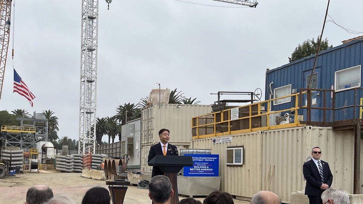 Rep Lieu speaking at a podium with construction equipment behind him