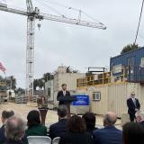 Rep Lieu speaking at a podium with construction equipment behind him